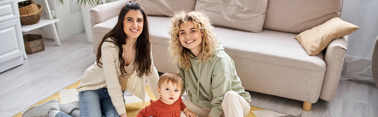 jolly lesbian couple playing with toys with their toddler daughter at home, modern parenting, banner