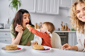 affectionate lesbian couple having breakfast with their small pretty daughter, family concept
