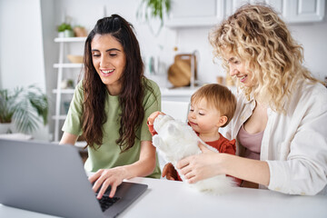 Fototapeta na wymiar nurturing lesbian couple in homewear watching movies with their baby girl on laptop, family concept