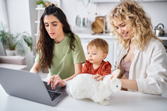 bonded lesbian couple in homewear watching movies with their baby girl on laptop, family concept