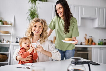 joyous charming lgbt couple in homewear having great time with their daughter at breakfast, family