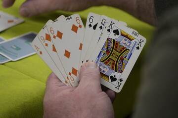 Hands of unrecognizable people play a game of bridge cards on a green table