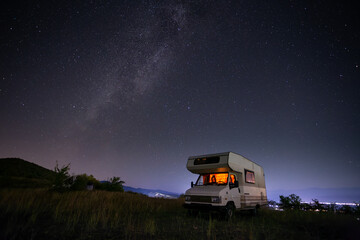 Motorhome, camper, at night under the starry sky next to a tree on a hill