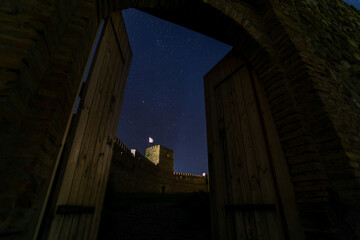 entrance to a medieval fortress at night, wooden gates, starry sky