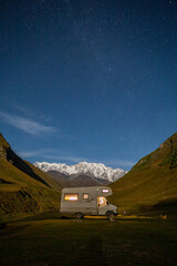 mobile home in the mountains against the backdrop of a snowy peak, starry sky