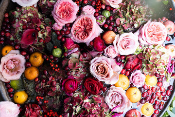 Red roses, hydrangea, reddish cranberries, chrysanthemums, tangerines in water in a tin basin as a...