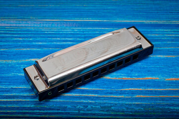 A metal harmonica with ten holes, a wind instrument, photographed on a wooden surface.
