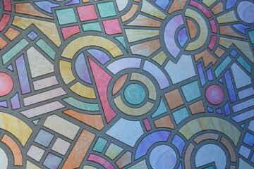 Unusual hand-drawn color film with a mosaic pattern glued to the glass of the balcony of an apartment. Graphic squares, circles, circles, and angles.