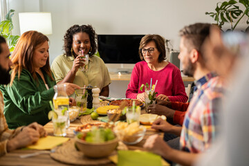 happy group of multicultural and different age friends celebrating dinner at home