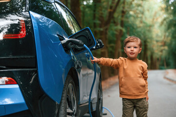 Obraz premium Cute young boy is charging the blue electric car outdoors