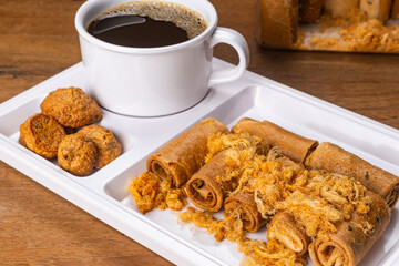 High angle view pile of sweet crispy coconut meringue and crispy coconut roll with dried shrodded pork and a cup of black coffee in plastic tray on wooden table.
