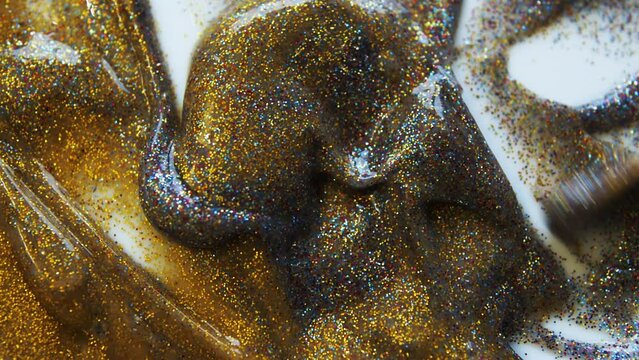 Texture of makeup cosmetics with sequins. Gold and pink liquid paint are flowing. Beautiful festive bokeh. Abstract background for Christmas. Liquid Brilliant Metallic Bronze Paint. Mix.