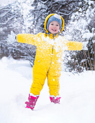 little smiling child in yellow clothes opening hands playing with snow on cold winter day in nature outdoors 