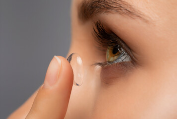 Beautiful young woman holding a contact lens on her finger. Eye care and choice of means to improve...