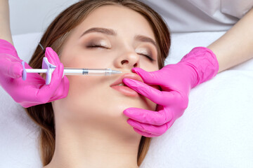 Cosmetologist does injections for lips augmentation of a beautiful woman. Women's cosmetology in...