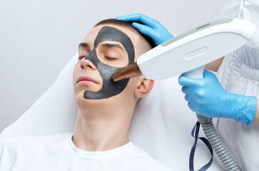 Beautician doing carbon peeling procedure to handsome guy in beauty salon. Hardware male...