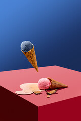 Levitating blueberry ice cream in waffle cone over cube with lying melting pink ice cream against...