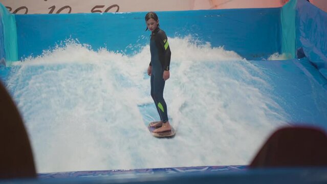 Indoor surf sports club for children. Theme is active recreation and extreme sports on water. Student and coach on surfing training on wave simulator. Teenager surfing board at water park.