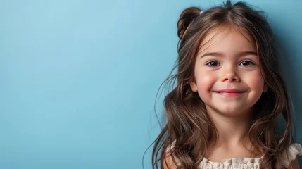 Foto op Aluminium Portrait of little pretty brunette hair girl child in dress with expression of joy on face, cute smiling isolated on a flat pastel blue background with copy space. Template for banner, text place. © SnowElf