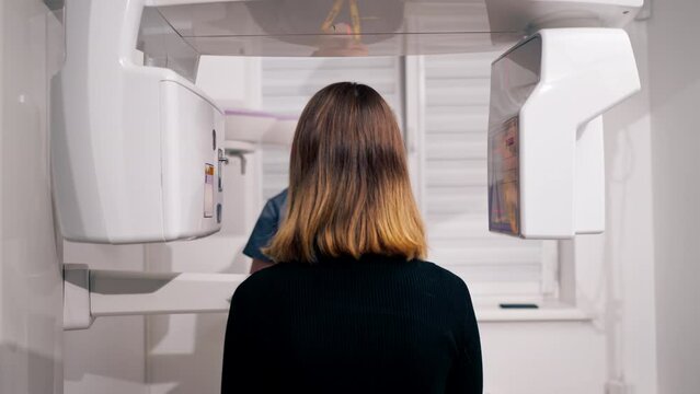 rear view of a woman doing a 3D scan of the nose and mouth in a plastic surgery clinic holding the device