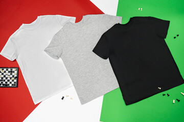 Close-up of the three t-shirts (black, white and grey) on color background redand green.