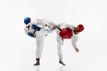 Two men in kimono and helmets practicing taekwondo, training, fighting isolated over white...