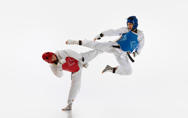 Dynamic image of young men, taekwondo athletes in kimono and helmets training isolated over white...