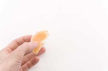 immagine con primo piano di mano ch regge spicchio di frutto di arancia sbucciata su superficie bianca - obrazy, fototapety, plakaty