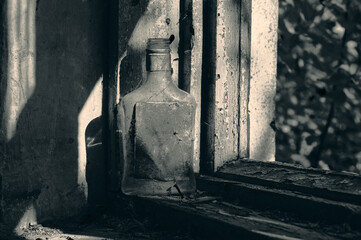 On the windowsill of an abandoned building there is an old dusty bottle of cognac, there is dirt...