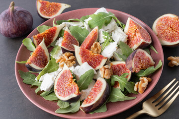 Tasty salad with sliced figs, crushed soft goat cheese, walnut and fresh arugula leaves on red...