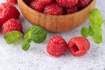 Fresh sweet raspberry berries with mint leaves on stone background.