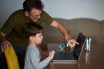 Father helps his son use a laptop. 