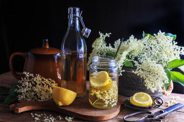 Homemade elderflower syrup and elderberry flowers on wooden table - dark and moody photography