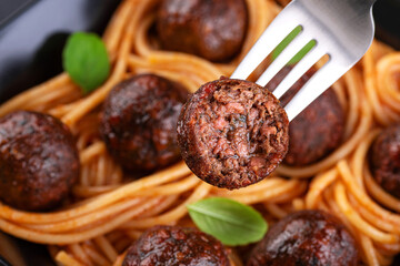 Fried vegan meatballs with noodles and basil leaves on a plate. Fork with half a meatball.