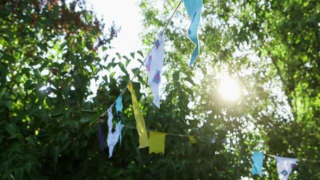 Hand Held Close Up Shot of String of colorful Fabric Flags in the Garden Against the Sun