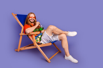 Full length photo of good mood man dressed print shirt lay on deckchair on vacation drink cocktail isolated on purple color background - obrazy, fototapety, plakaty