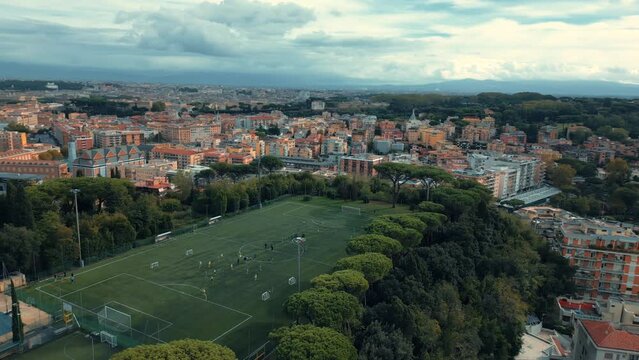 Cancha de futbol deporte personas haciendo ejercicio jugando en la ciudad de roma vista aérea vuelo de lateral drone lleno de árboles con el cielo nublado al atardecer y con mucho césped