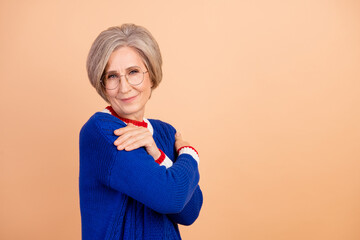 Photo of pleasant cheerful senior woman with gray hair dressed knitwear warm sweater arms hug herself isolated on beige color background