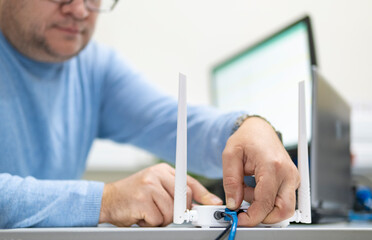 A man connects a cable to the router's Wi-Fi port while sitting at a desk in the office.