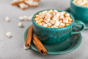 Hot drink with marshmallows and candy cane in blue cup on texture table.Cozy seasonal holidays.Hot cocoa with gingerbread Christmas cookies.Hot chocolate with marshmallow and spices.Copy space.