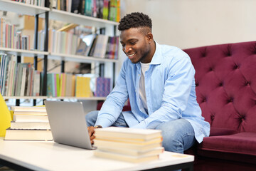 Obraz premium A happy and focused student utilizing a laptop for studying and research in a modern library setting.