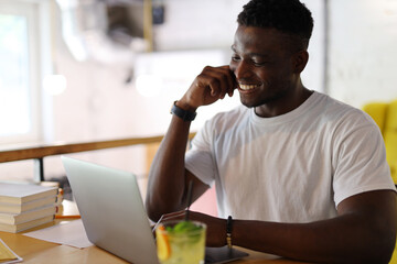 A young man working on a laptop in a cafe, enjoying a cup of coffee while using technology in a casual and comfortable environment.