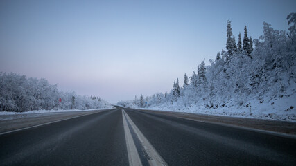 A desolate highway stretches through a snowy forest landscape, evoking concepts of winter travel...