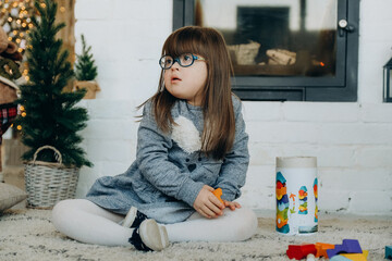 A little girl with Down syndrome plays in the house near the fireplace on Christmas Eve.