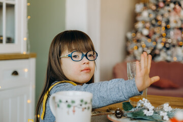A girl with Down syndrome drinks orange juice and sits at the table on Christmas Eve.