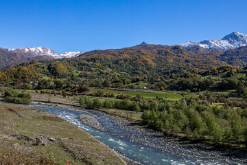 A serene landscape showcasing a meandering river with autumn-colored forests and snow-capped mountains, exemplifying rural beauty and the change of seasons