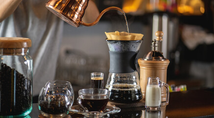 Fototapeta na wymiar drip coffee, Barista making drip coffee by pouring spills hot water on coffee ground with prepare filter from copper pot to glass transparent chrome drip maker on wooden table in cafe shop