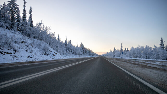 A tranquil winter road scene with snow-covered trees lining the highway at dusk, suggesting themes of travel, solitude, or wintry landscapes