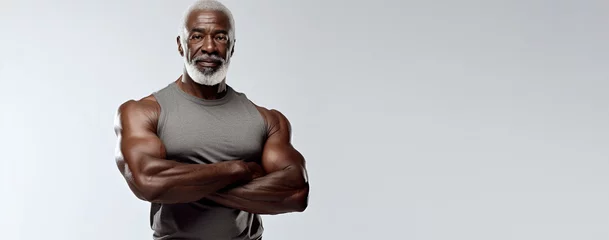 Foto op Canvas Athletic muscular elderly African American man stands with crossed arms against white background. Advertising banner layout for a gym or fitness trainer. © OleksandrZastrozhnov
