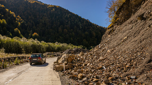 A lone car navigates a mountain road partially obstructed by a rockslide, exemplifying concepts of danger and unpredictability in nature